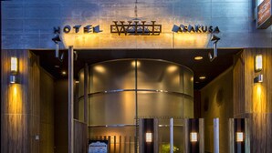 La entrada del Hotel Will City Sakusa, con un diseño moderno, presenta una puerta de vidrio curva y señalización iluminada.