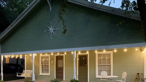A green house with a porch, string lights, a compass decoration, and a number 508 on the wall. - Compass Cottage in Historic Glen Rose (Glen Rose)