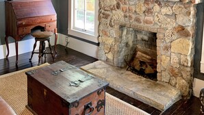 A room with a stone fireplace, a wooden desk, a flat-screen TV, and a window with a view of greenery. - Compass Cottage in Historic Glen Rose (Glen Rose)