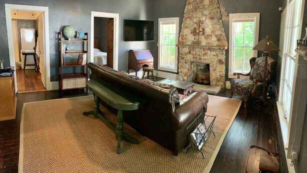 A living room with a stone fireplace, a large flat-screen TV, a leather sofa, and a bookshelf. - Compass Cottage in Historic Glen Rose (Glen Rose)