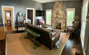 A living room with a stone fireplace, a large flat-screen TV, a leather sofa, and a bookshelf.