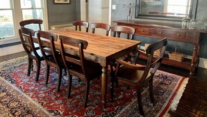 A dining area with a wooden table and chairs, a patterned rug, and a view of the outdoors through large windows. - Compass Cottage in Historic Glen Rose (Glen Rose)