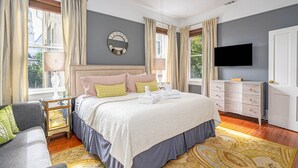 Een slaapkamer met een groot bed, een dressoir, een televisie en een raam met gordijnen.