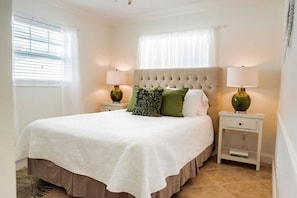 A neatly arranged bedroom with a large bed, two bedside tables, and a window with blinds.