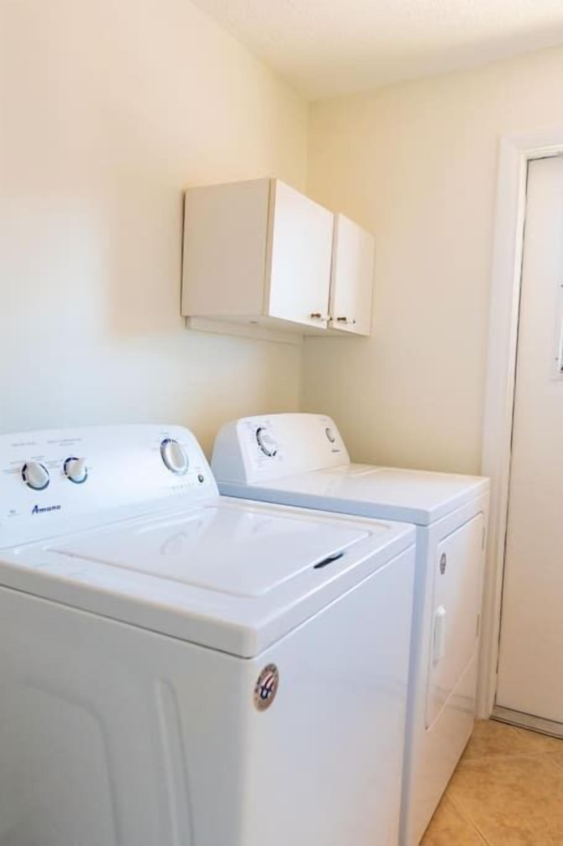 Une buanderie avec deux machines à laver blanches, un meuble de rangement au-dessus et une porte sur la droite.