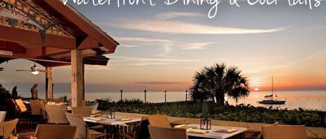 An outdoor dining area with tables and chairs, overlooking a sunset view.