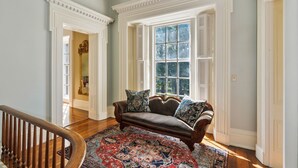 Une pièce avec un canapé en cuir marron, un tapis à motifs et une grande fenêtre avec des volets.