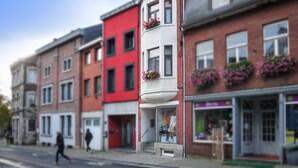 Un immeuble à plusieurs étages, doté d’une façade rouge et blanche, abritant un commerce au rez-de-chaussée avec une entrée bien visible et un petit espace extérieur aménagé en terrasse.