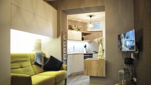 Un salon moderne avec un canapé jaune, une table basse en bois et un téléviseur fixé au mur.
