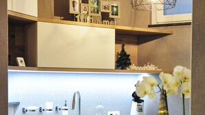 Une cuisine moderne avec un plan de travail blanc, un évier, une machine à café et un vase rempli de fleurs.