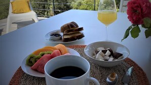 Una mesa con alimentos para el desayuno, incluyendo tostadas, fruta, un vaso de jugo y una taza de café, con un paisaje pintoresco de fondo.
