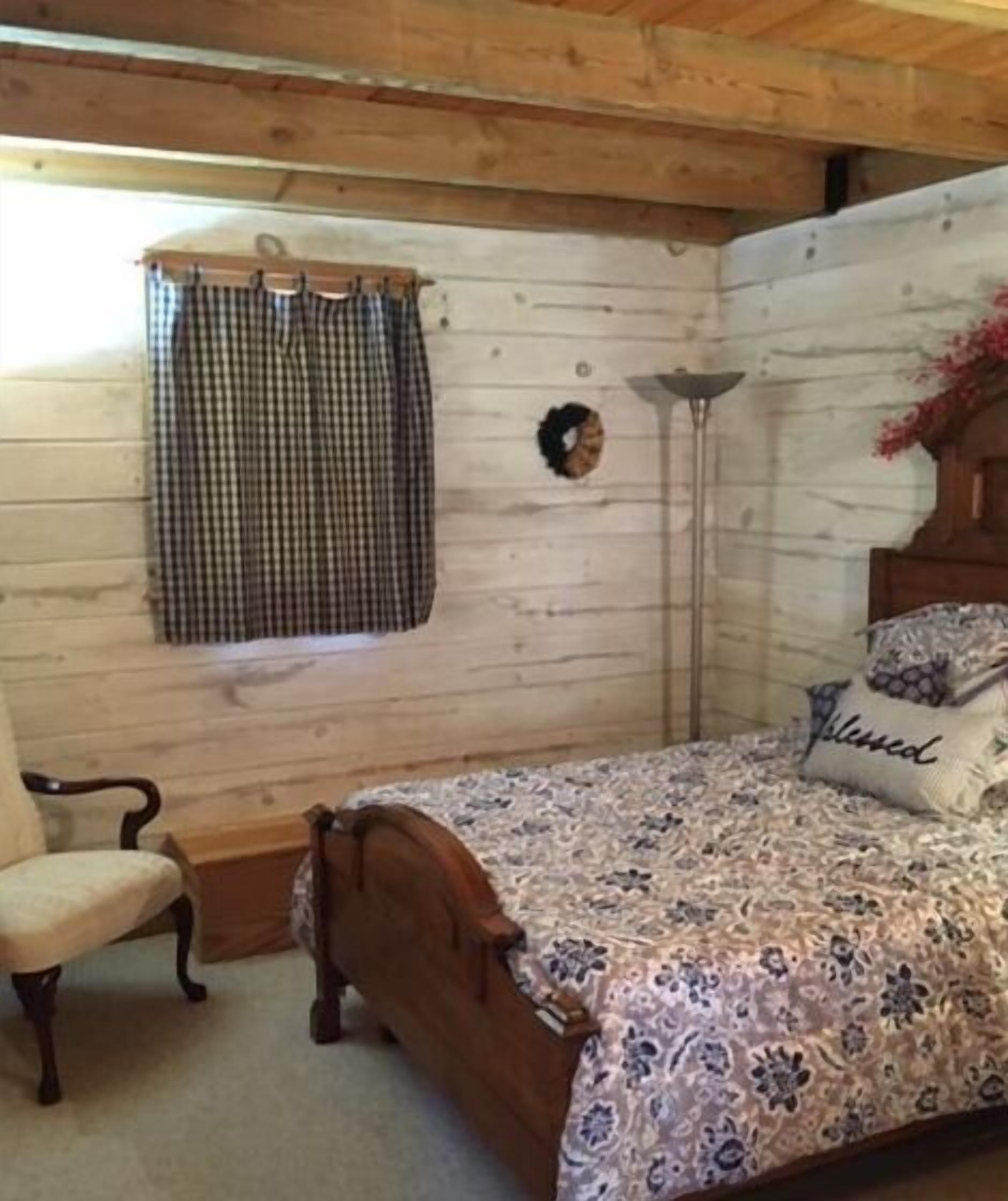 Une chambre à coucher avec une tête de lit en bois, une couvre-lit à motifs, une chaise et une fenêtre ornée de rideaux à carreaux.