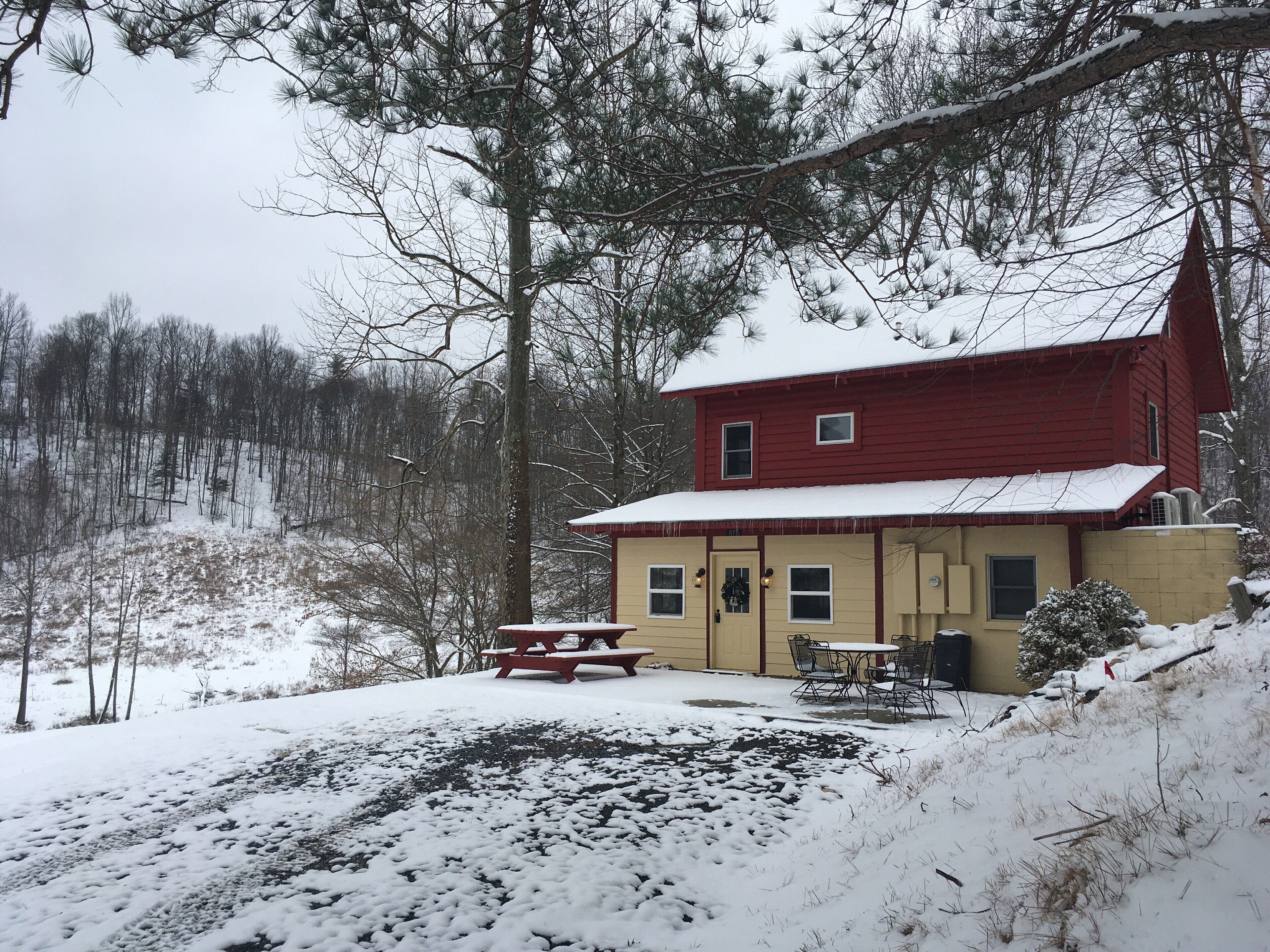 Une maison rouge à deux étages, dont le toit est recouvert de neige, et devant laquelle se trouve une table de pique-nique.