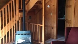 En interiör med träpanel, en trappa, en öppen spis och en röd stol.
