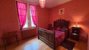 Ein Schlafzimmer mit einem hölzernen Bett, einem Nachttisch, einer Lampe und einem Fenster mit rosa Vorhängen.