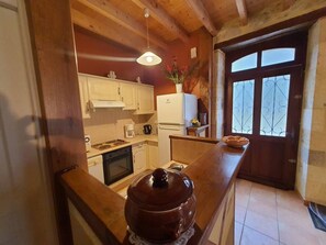 A compact kitchen with wooden cabinets, a stove, a refrigerator, and a large pot on the counter.