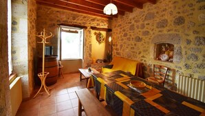 A rustic dining area with a wooden table and benches, stone walls, a wooden ceiling, and a hanging light fixture. - Gîte Nico Label Pêche - 4 pers proche du Gers (LANNES)