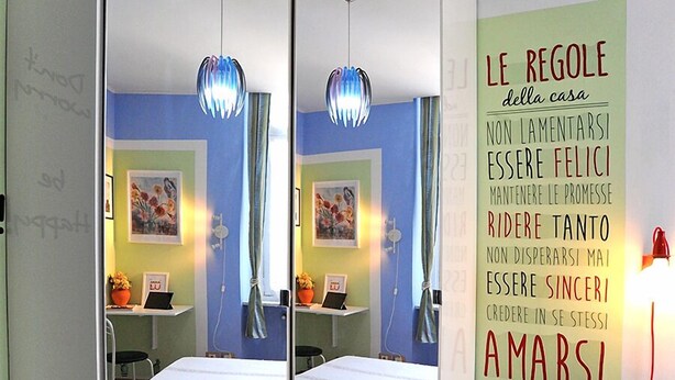 A bedroom with a bed, a mirror, a bedside table, and a wall with motivational text. - Uno sguardo su Porta Palazzo (Turin)