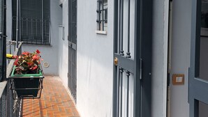 A narrow alleyway with a green wheelbarrow of flowers, a metal gate, and a window with blinds. - Uno sguardo su Porta Palazzo (Turin)