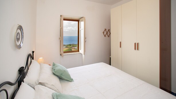 A bedroom with a bed, a window with an open view, a wardrobe, and a bedside table with a lamp. - Casa Gallizza by Wonderful Italy (Cefalù)
