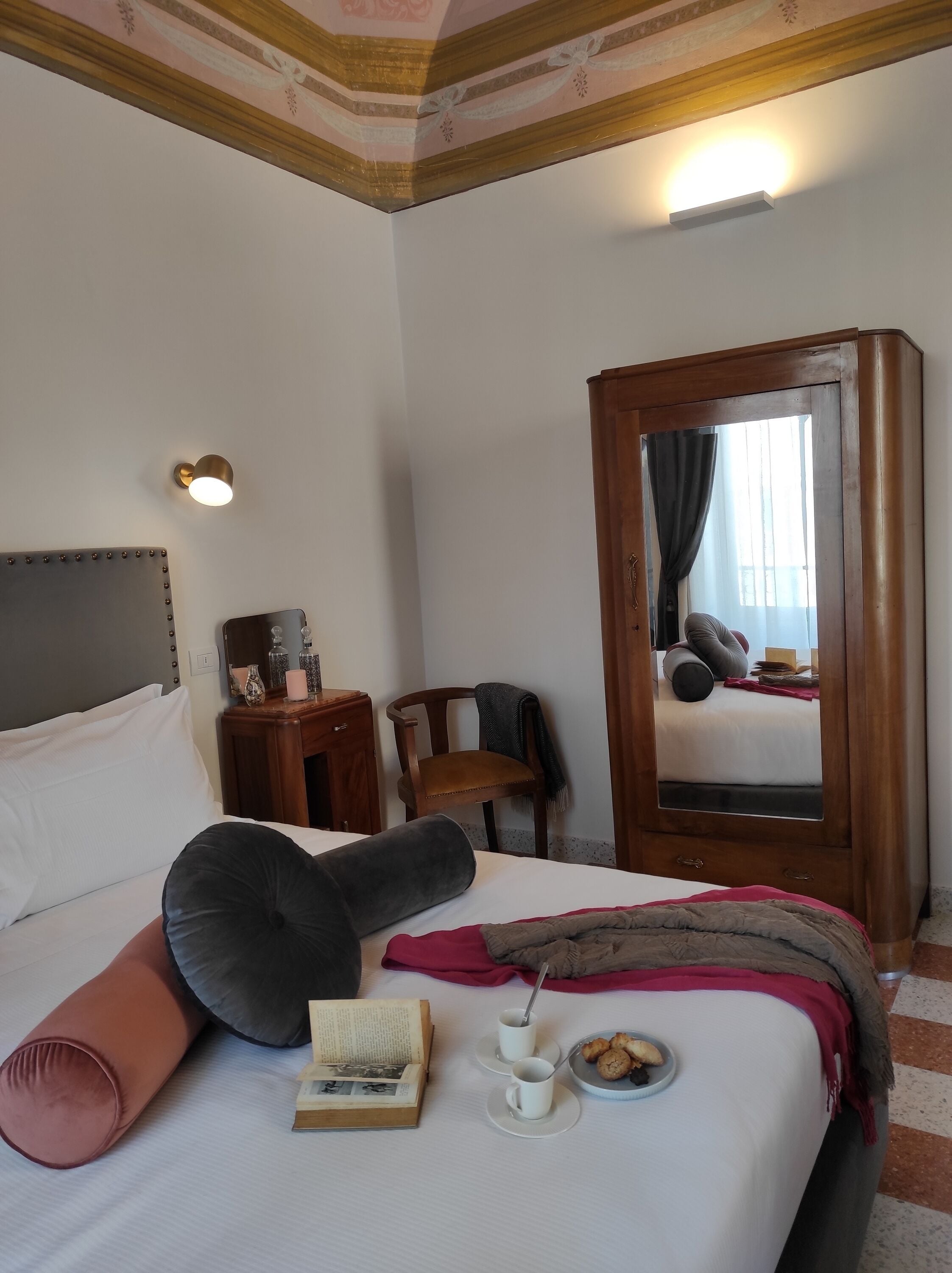 A hotel room with a bed, a bedside table, a chair, a mirror, and a window with curtains.