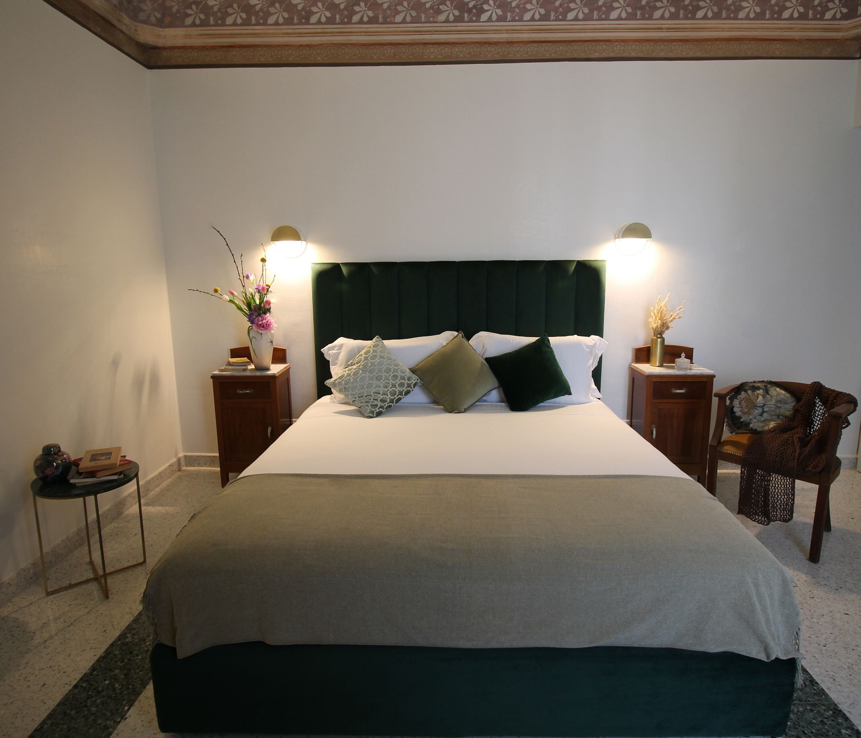 A neatly made bed with a dark headboard, two bedside tables with lamps, and a small side table with a vase of flowers.