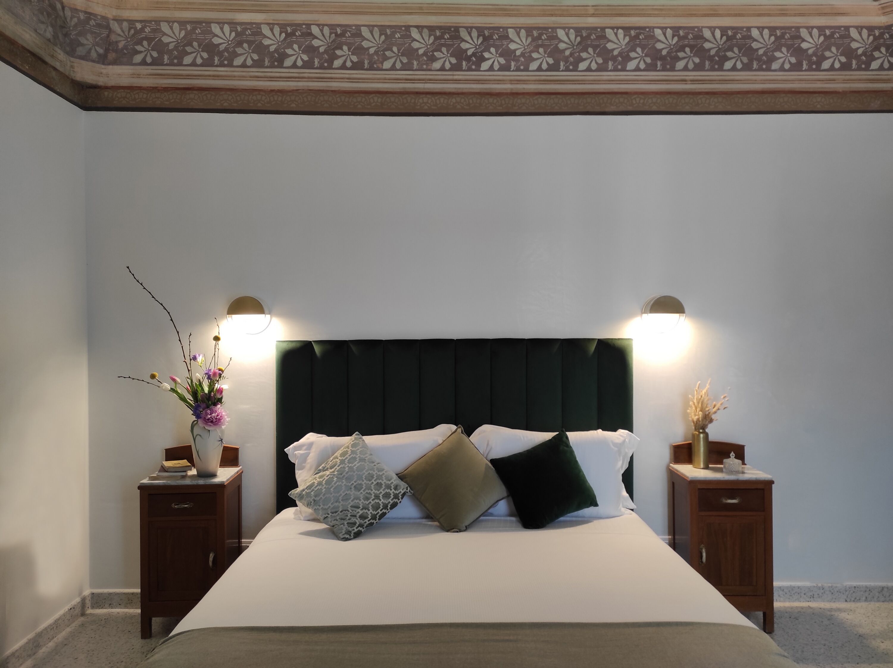 Un lit bien fait, avec une tête de lit sombre, flanqué de deux tables de chevet sur lesquelles sont posées des lampes, dans une pièce au design simple et épuré.