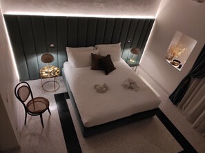 A modern hotel room with a large bed, two bedside tables with lamps, a chair, and a decorative wall piece. - 1940 Luxury Accommodations by Wonderful Italy (Ostuni)