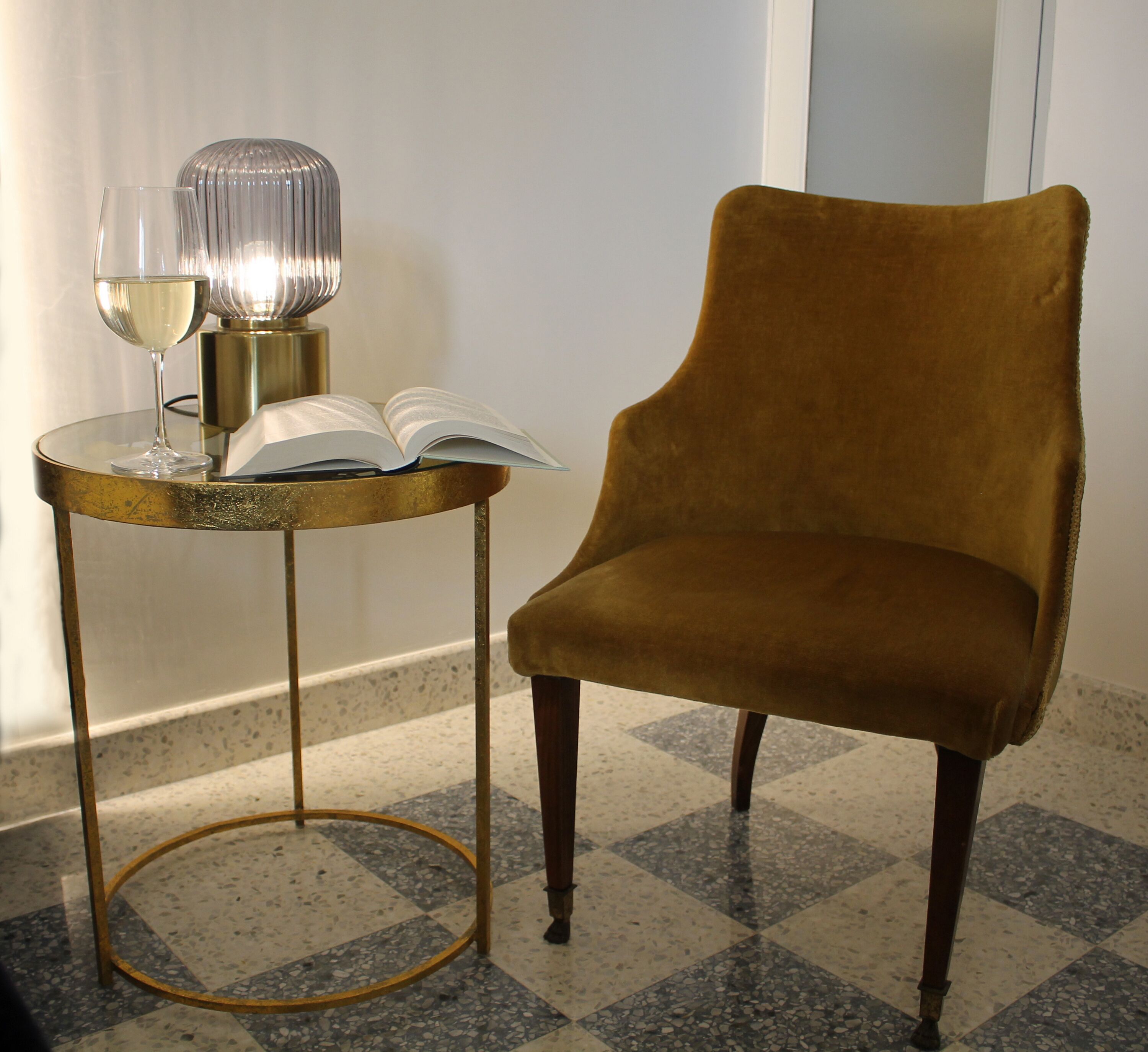 Una habitació amb un terra de pissos, una taula rodona amb un llibre i un got de vi, i un armchair de vellut.