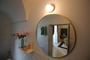 A bathroom with a round mirror, a shelf with a vase of flowers, and a white tiled wall.