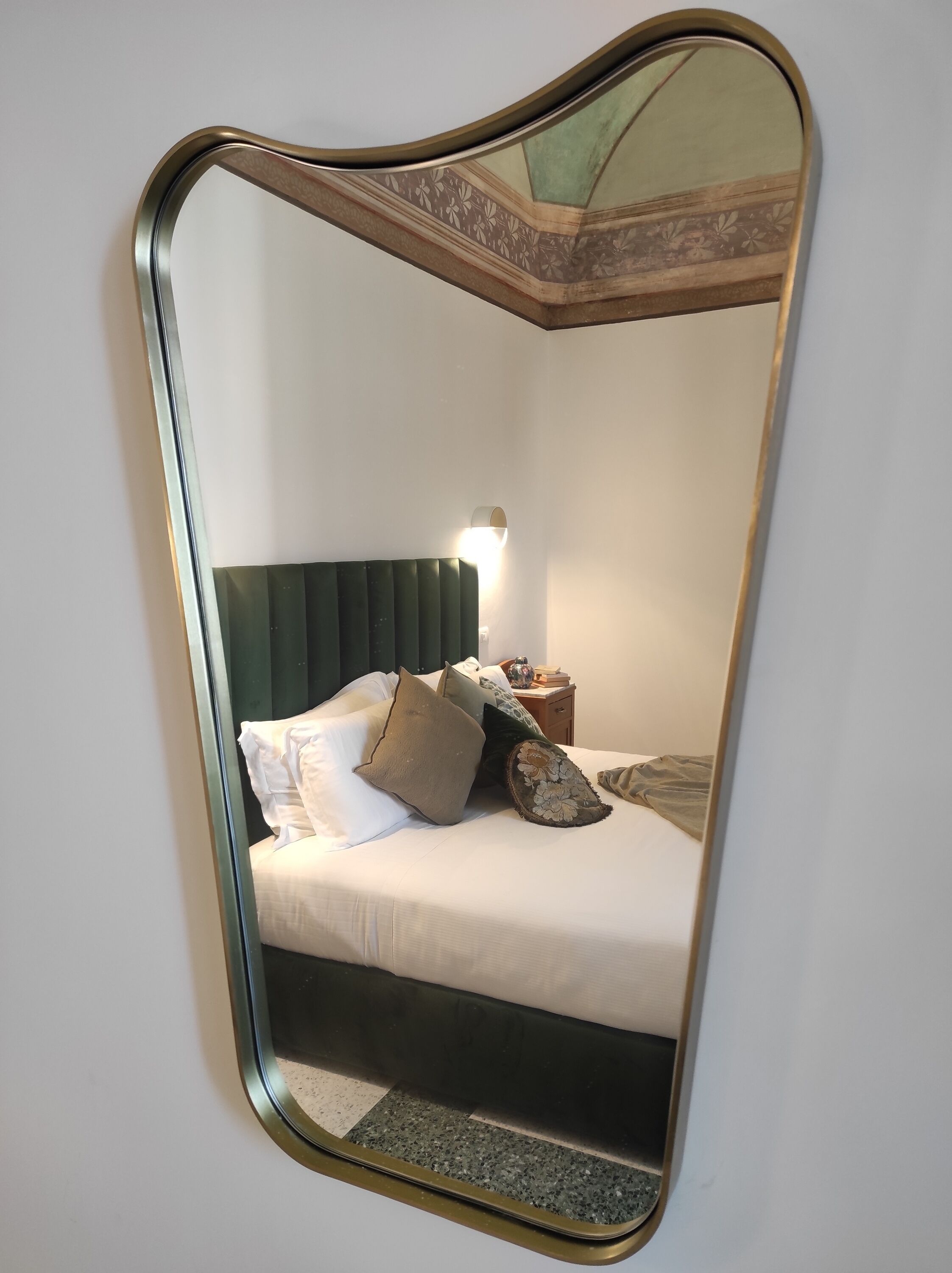 A bedroom with a bed, pillows, a nightstand, and a wall-mounted mirror.