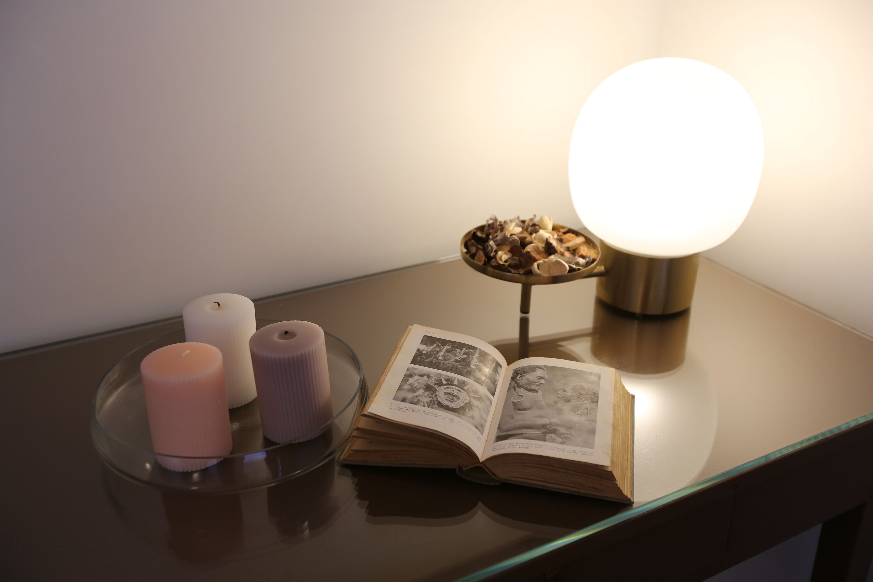 Une table de chevet avec un livre, deux bougies et une lampe décorative.