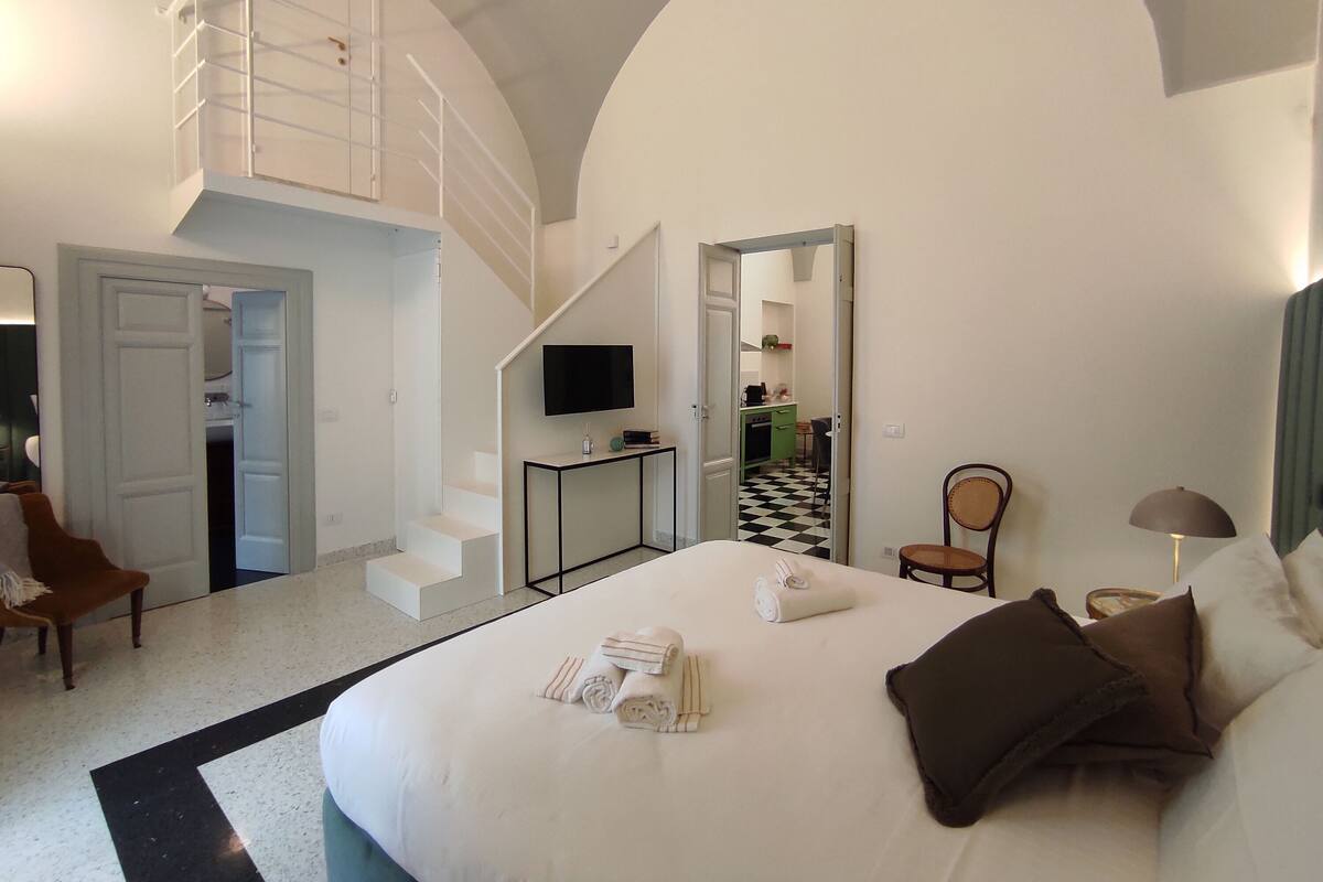 Une chambre d’hôtel avec un grand lit, une télévision, un bureau et un escalier menant à un étage supérieur.