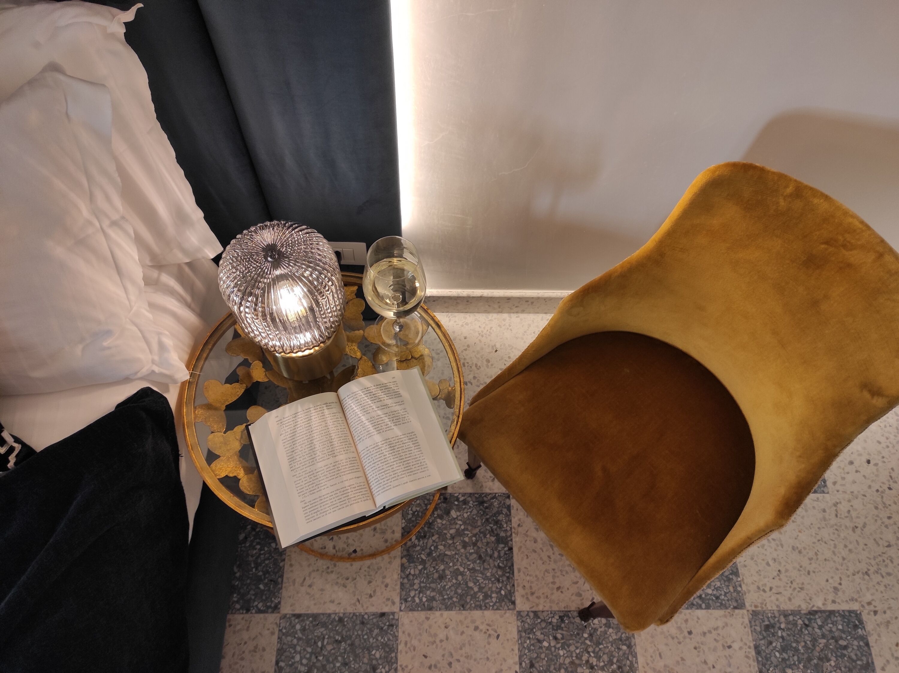 Una cama con sábanas blancas, una mesita de noche con un libro, una lámpara y un vaso de agua.