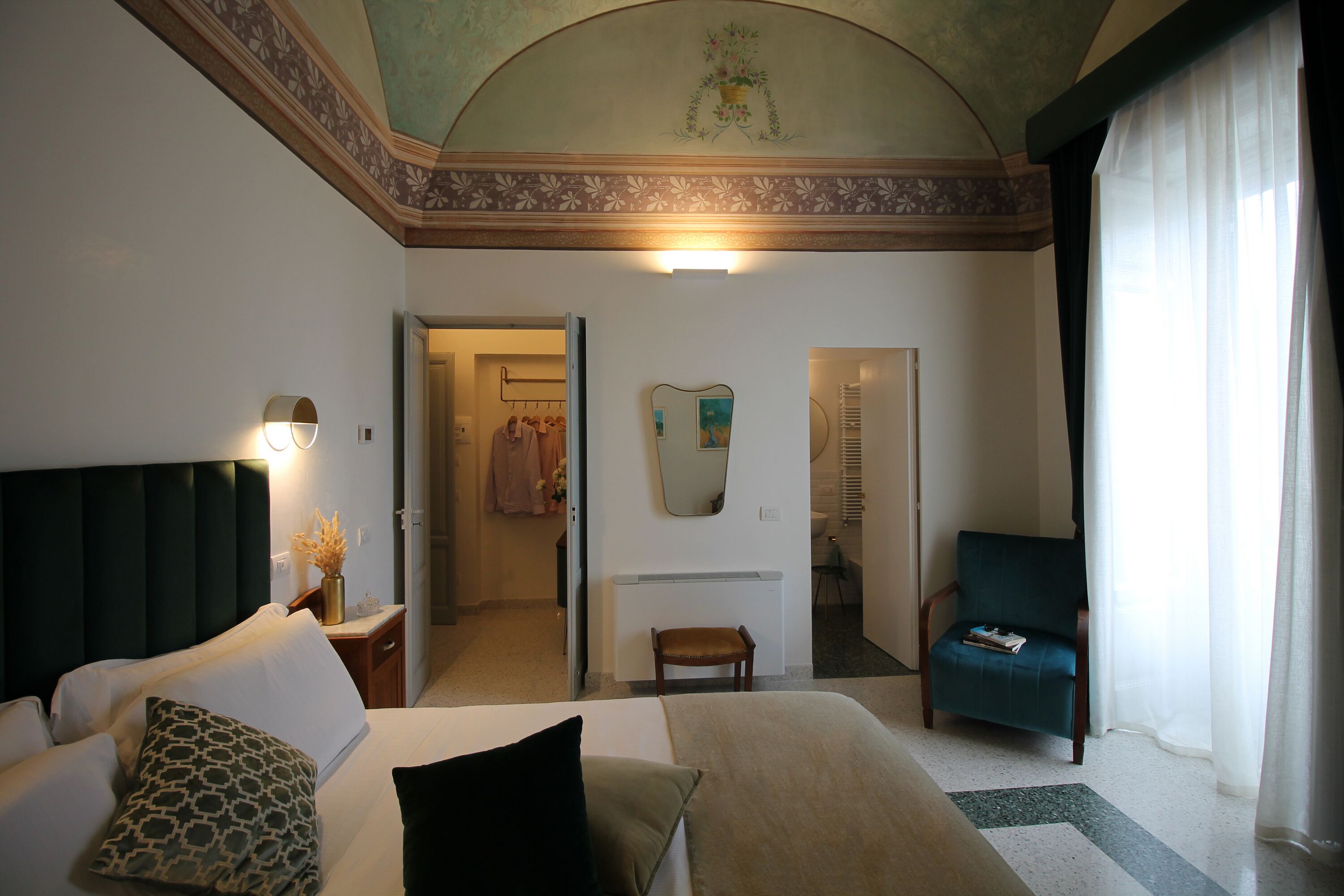 A hotel room with a bed, a chair, a mirror, and a view of a bathroom.
