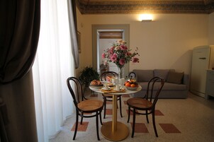 A dining area with a round table, four wicker chairs, a vase of flowers, and a sofa in the background.
