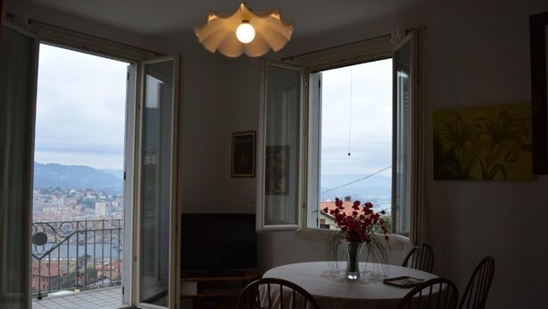 A dining area with a table and chairs, a vase with flowers, and a TV on a stand. - Charme and Comfort near Cinque Terre by Wonderful Italy (La Spezia)
