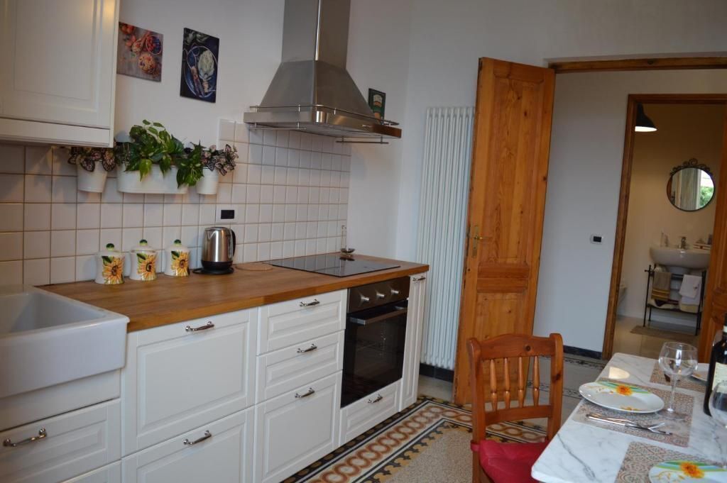 Een compacte keuken met witte kastjes, een inbouwoven, een rvs afzuigkap en een klein aanrecht met een waterkoker en decoratieve objecten.