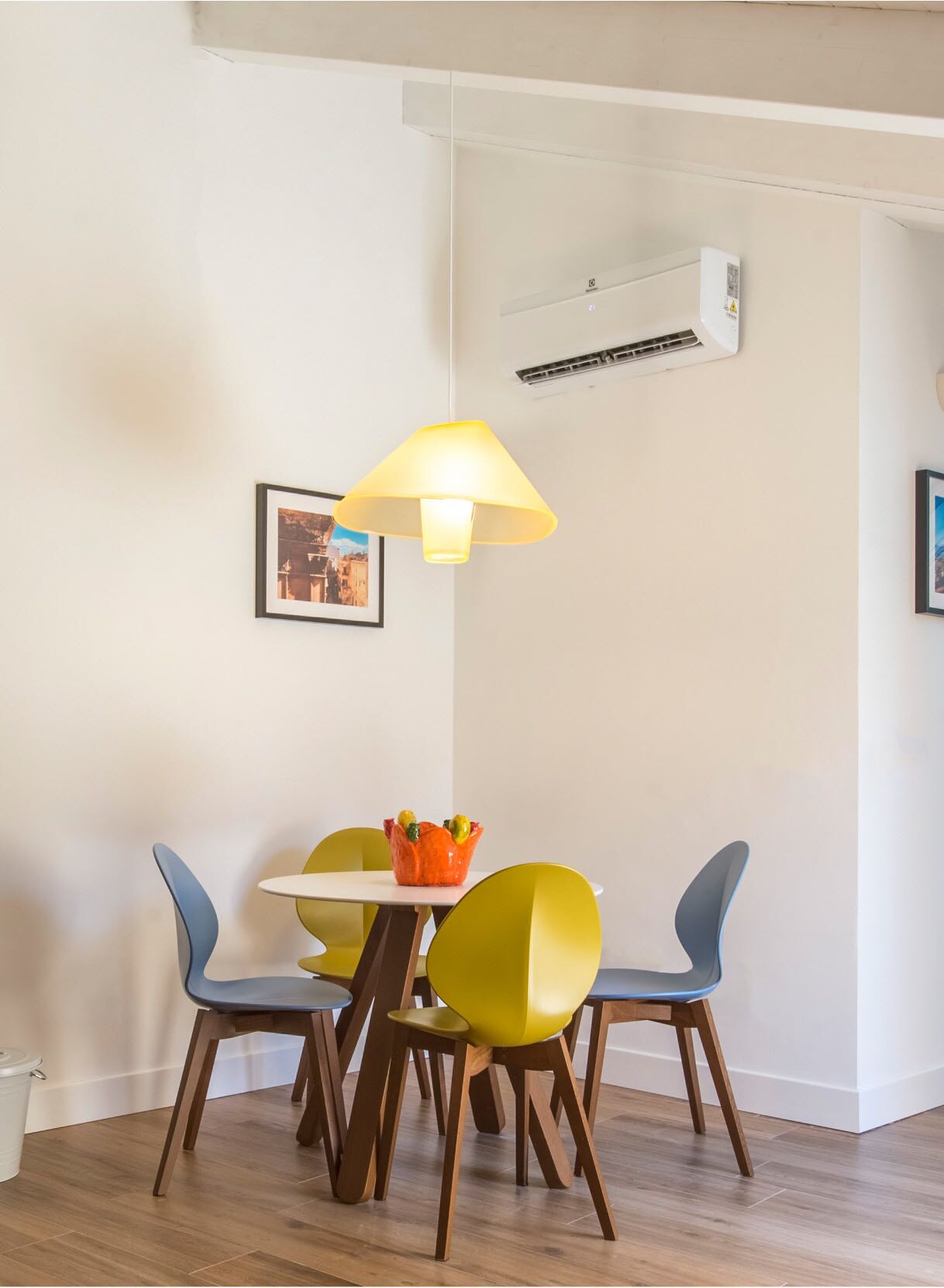 A dining area with a table and four chairs, an air conditioner, and a wall-mounted lamp.