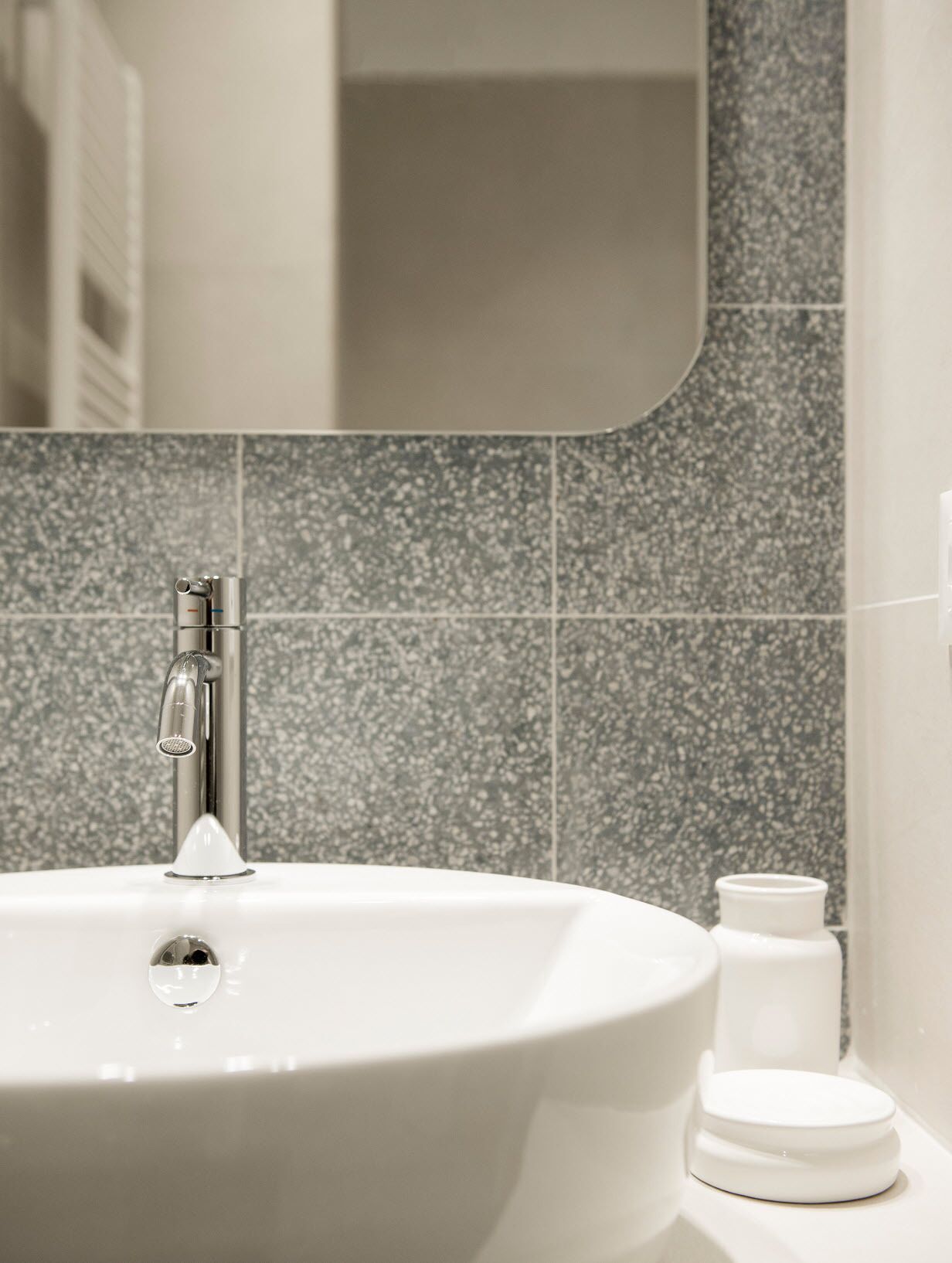 Un bagno con un lavandino bianco, uno specchio e una parete rivestita di piastrelle.