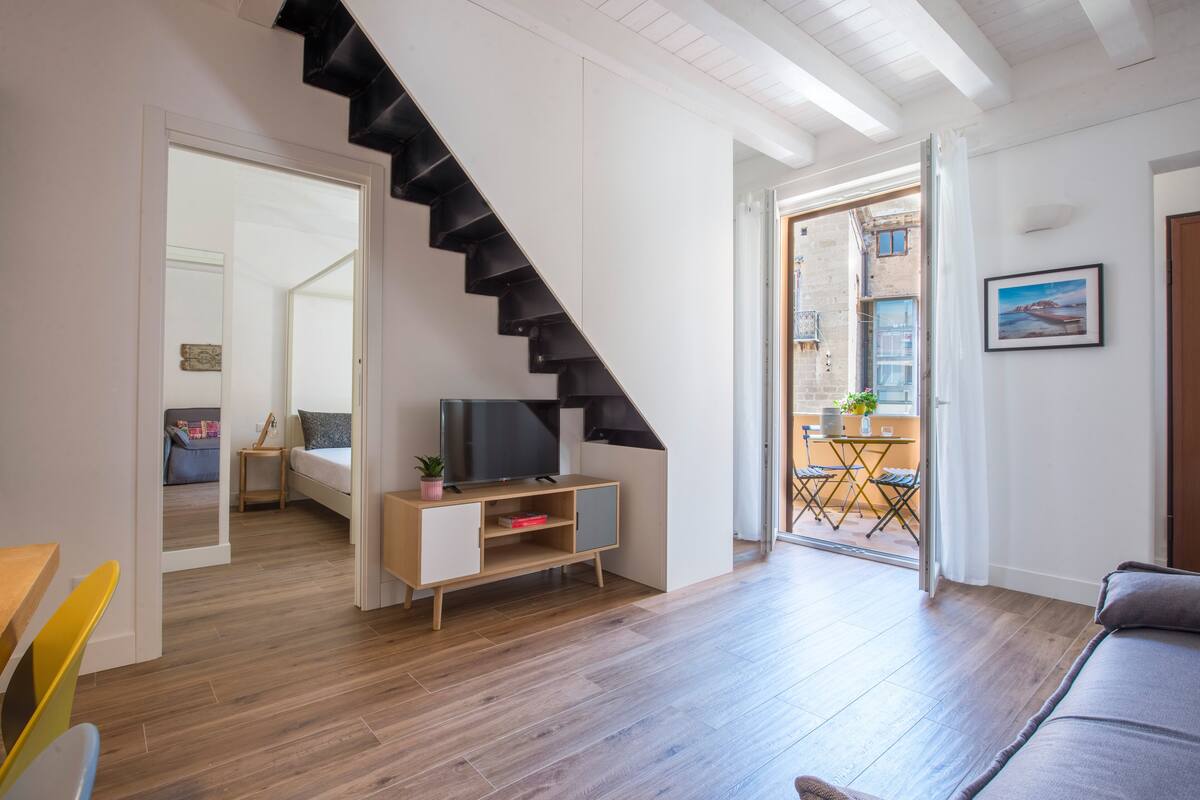 Een moderne woonkamer met een trap, een televisie en een balkon.