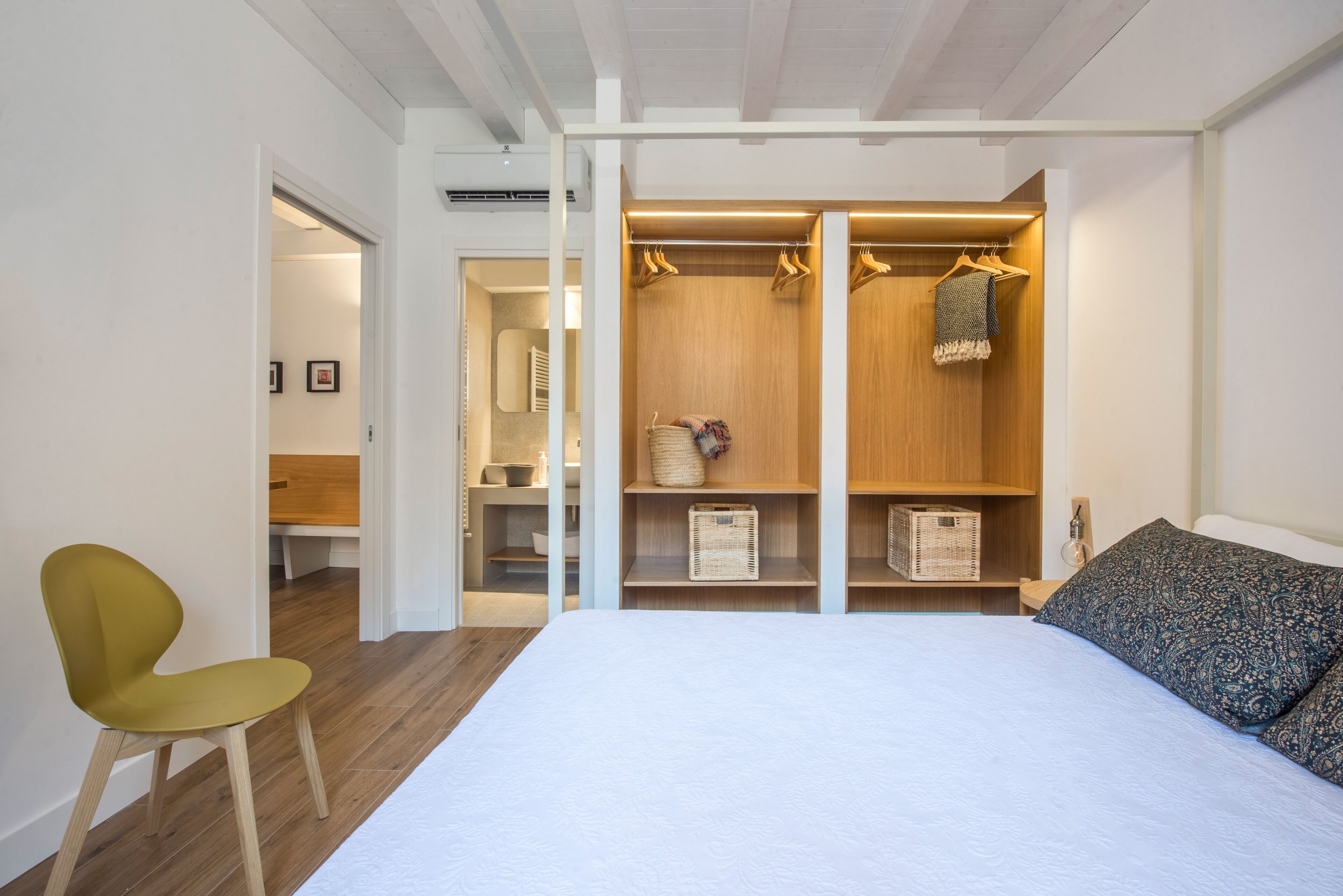 Une chambre à coucher comprenant un lit, une chaise, un dressing avec des étagères en bois et des cintres, et une petite table de chevet.