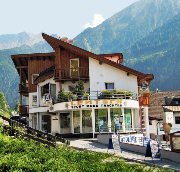 A building with a sign reading "Sport Mode Trachten" and "Restaurant Pitzlhaus" in front of a mountainous backdrop.
