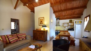 A cozy living room with a sofa, a wooden coffee table, and a dining table with chairs. There is a kitchen area with a stove, microwave, and refrigerator.