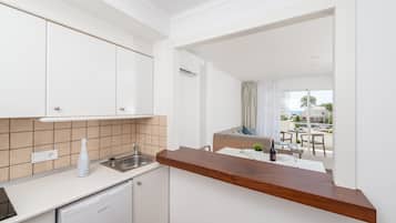Eine kleine Küche mit weißen Schränken, einer Holz Arbeitsplatte und Blick auf einen Außenbalkon mit Tisch und Stühlen.