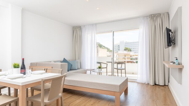 Ein modernes Hotelzimmer mit Essbereich, einer Couch, einem Balkon mit Blick und einem an der Wand befestigten Fernseher.