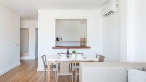 Ein moderner, minimalistischer Essbereich mit einem weißen Tisch, gedeckt für vier Personen, Holzboden und einem neutralen Sofa im Vordergrund.