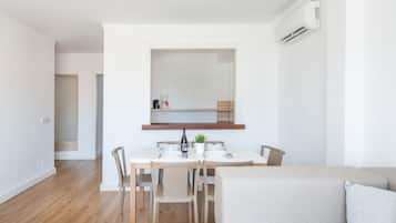 Ein moderner, minimalistischer Essbereich mit einem weißen Tisch, gedeckt für vier Personen, Holzboden und einem neutralen Sofa im Vordergrund.