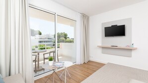 Una sala de estar moderna con un amplio ventanal corredero que da a un balcón, un televisor de pantalla plana montado en la pared y una pequeña mesa con una revista.