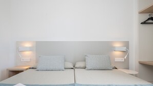 Una cama doble con dos almohadas, una mesita de noche con lámpara y una lámpara de pared.